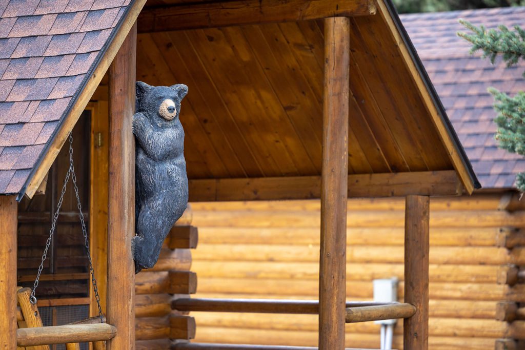 A wooden sculpture of a black bear hangs from an exterior post on the porch of a log cabin at Snake River Cabins.