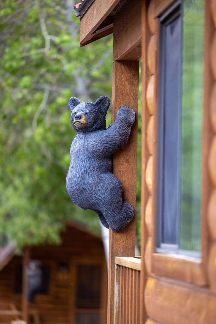 A wooden sculpture of a black bear hangs from an exterior post on the porch of a log cabin at Snake River Cabins.