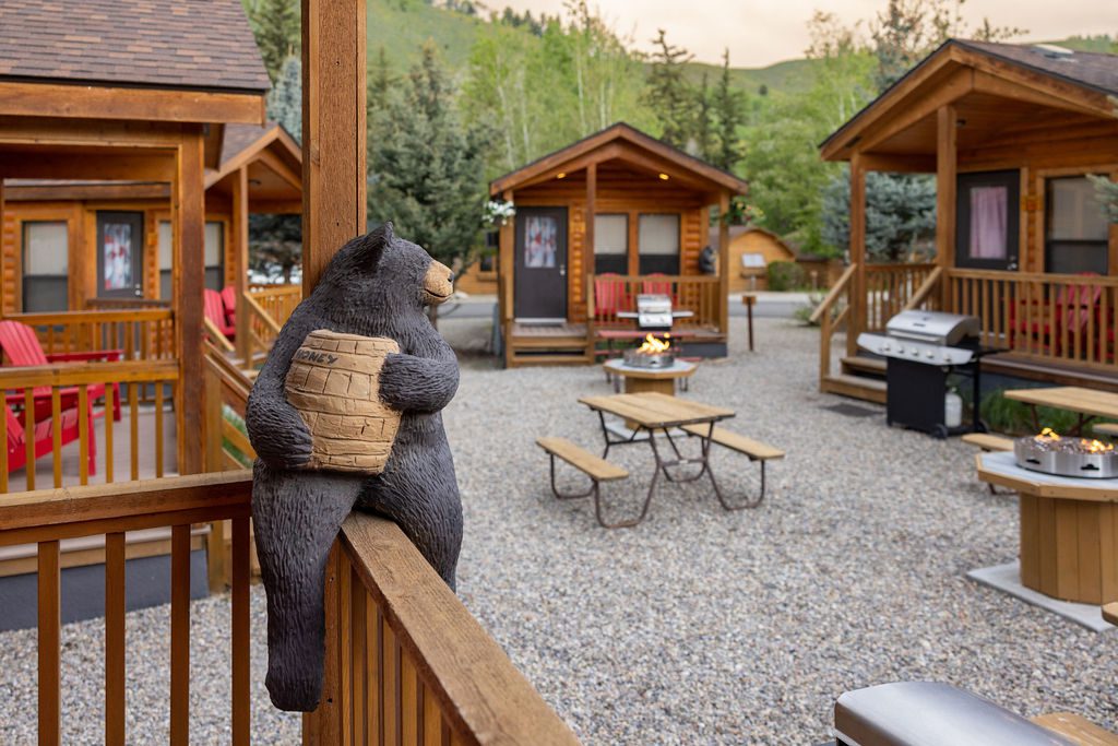 A wooden sculpture of a black bear holding a jar of honey sits on the porch of a log cabin at Snake River Cabins.