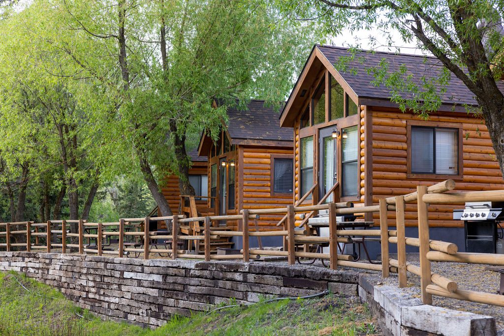 A log cabin with a grill under large trees at Snake River Cabins.