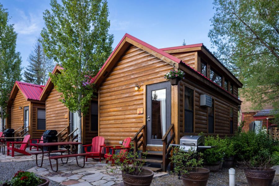 Three log cabins with red Adirondack chairs, picnic tables and grills at Snake River Cabins.