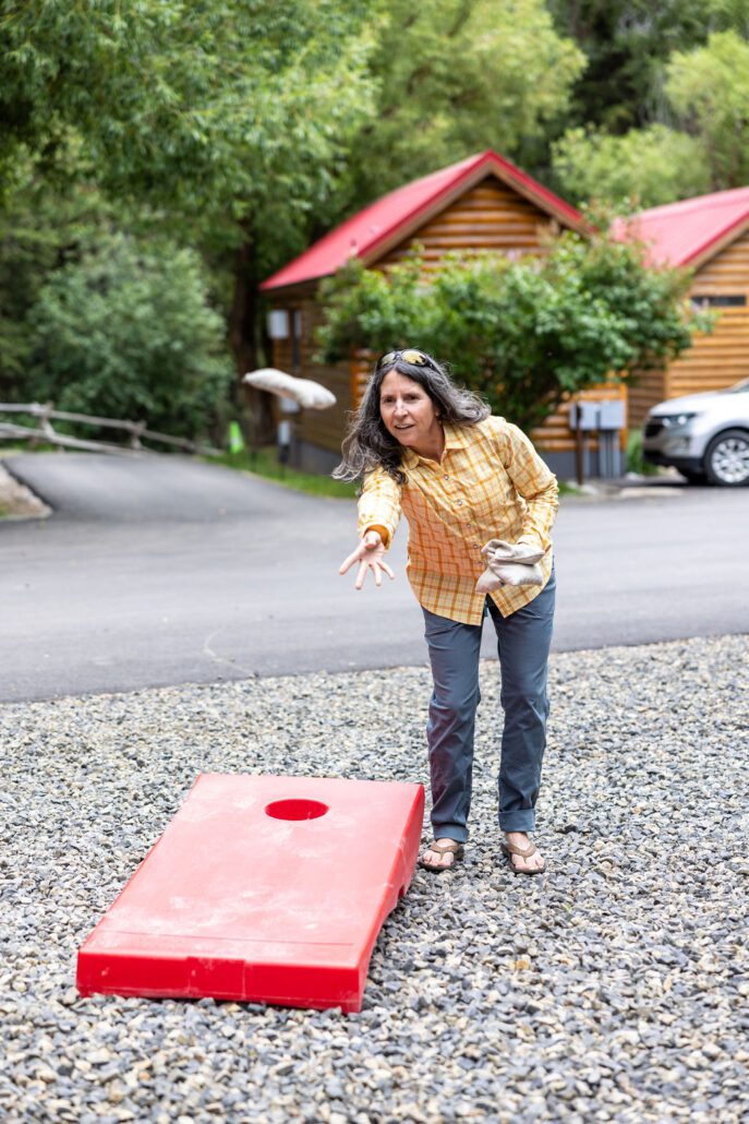 A woman in a yellow shirt throws a bean bag while playing a lawn game at Snake River Cabins.