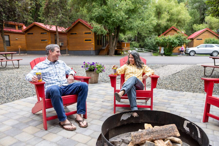 A man and woman sit in red Adirondack chairs in a common space at Snake River Cabins.