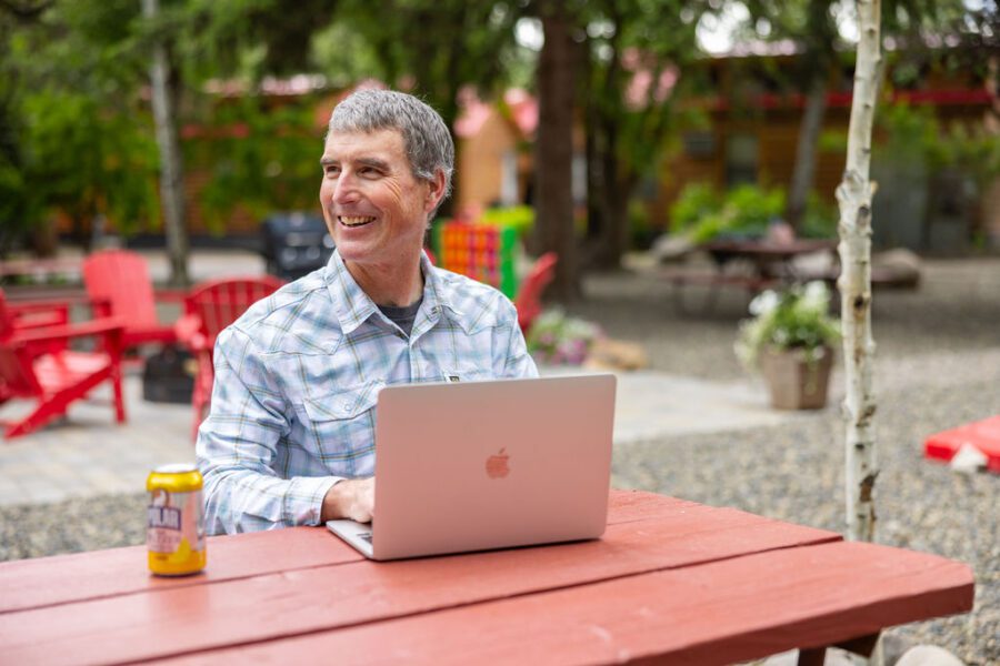 A man works on his silver laptop from a picnic table at Snake River Cabins.