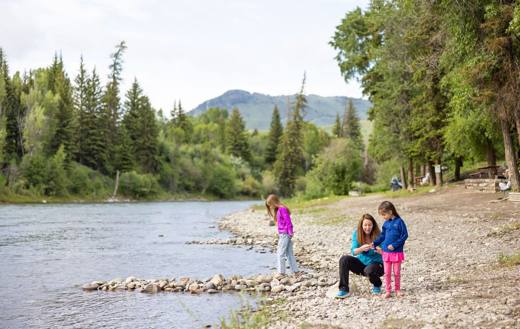 A family of four play on pebbled riverbank at Snake River Cabins.