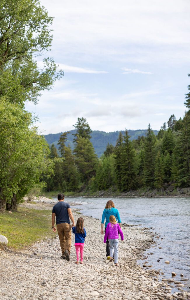 A family of four hike along a pebbled riverbank at Snake River Cabins.