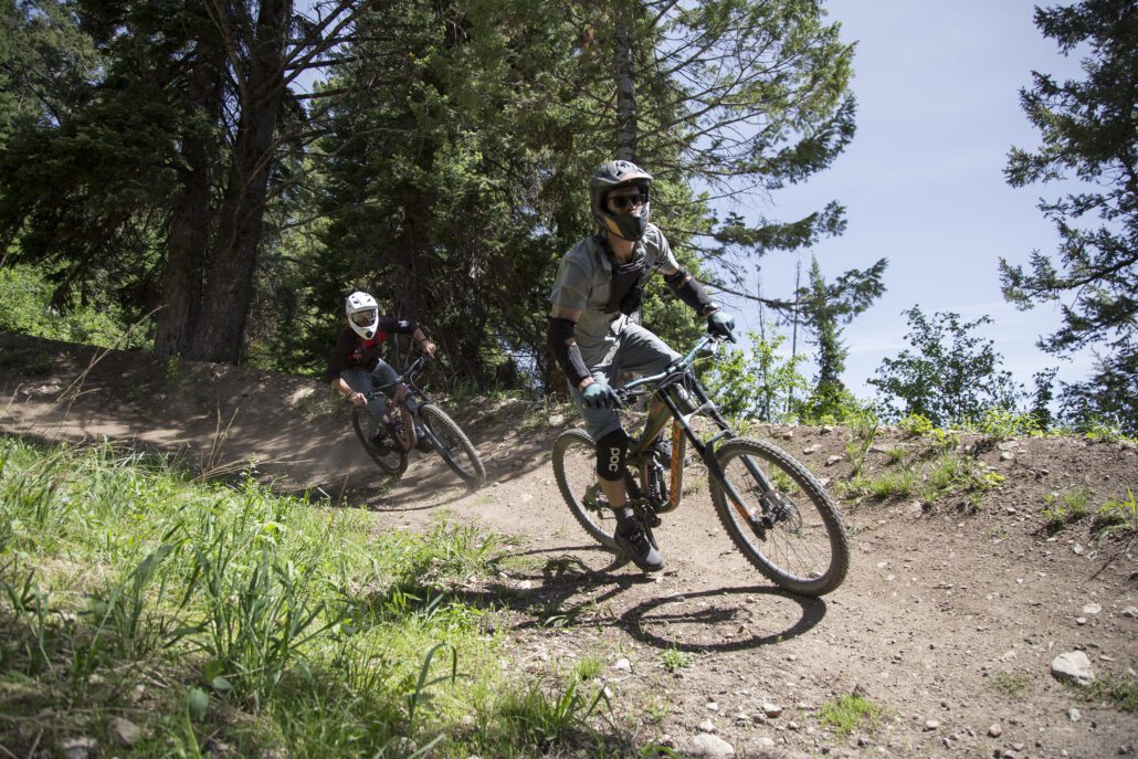 Two downhill mountain bikers crest a banked turn at Jackson Hole Mountain Resort.